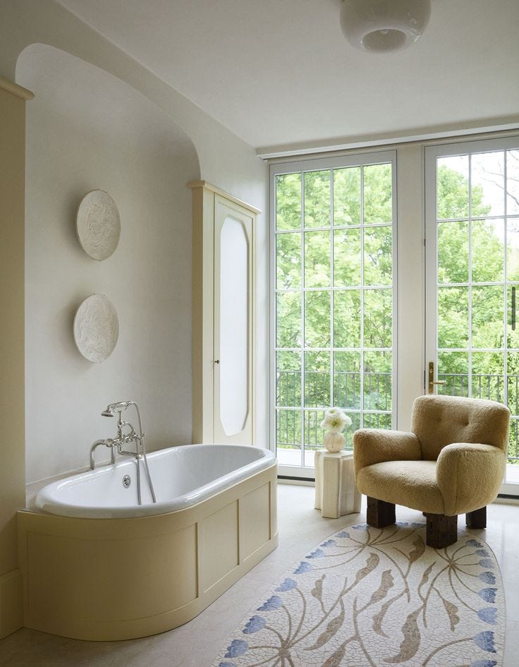 This may contain: a bathroom with a tub, chair and large window