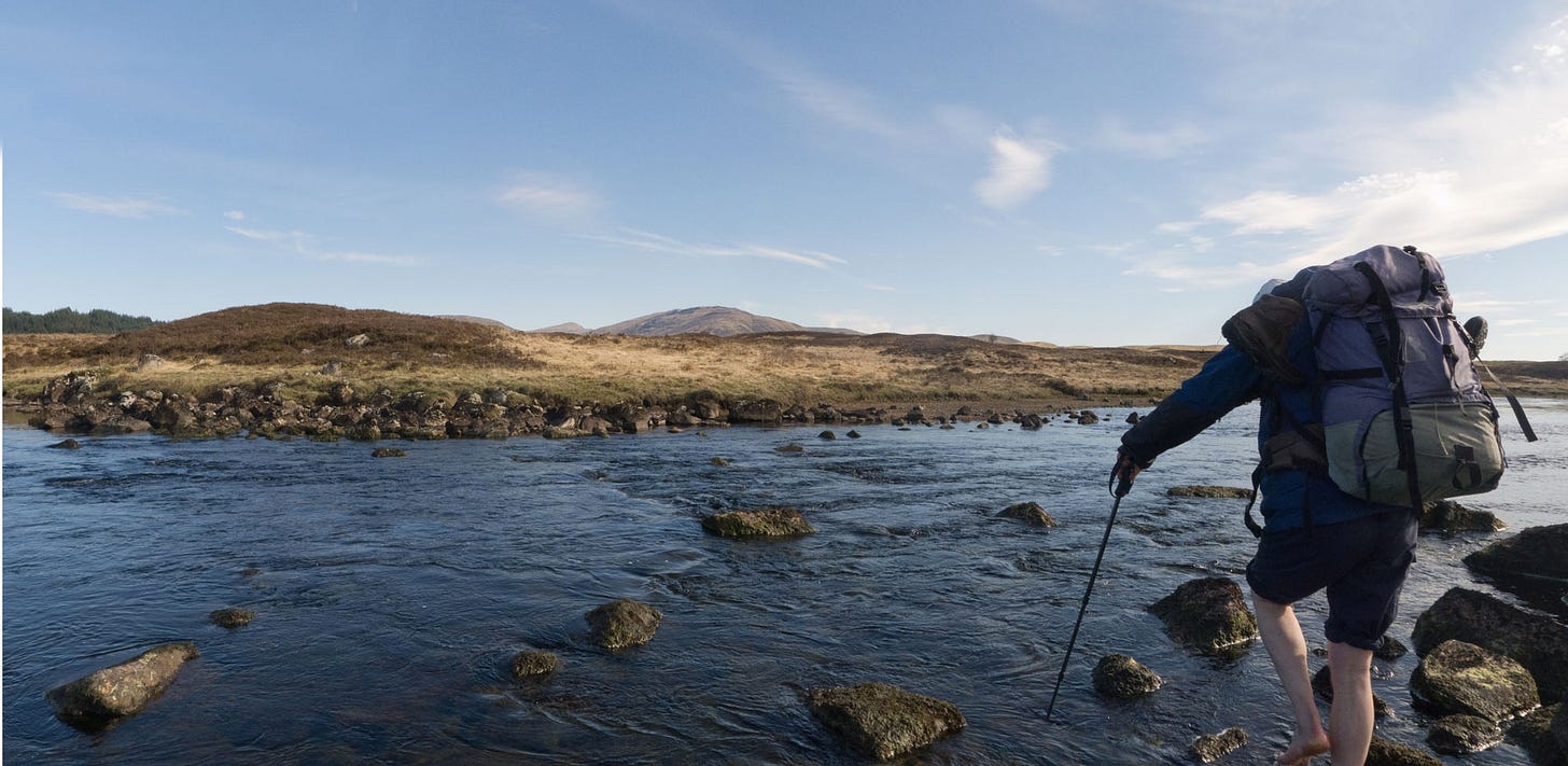 Person with big backpack crossing wide, shallow river