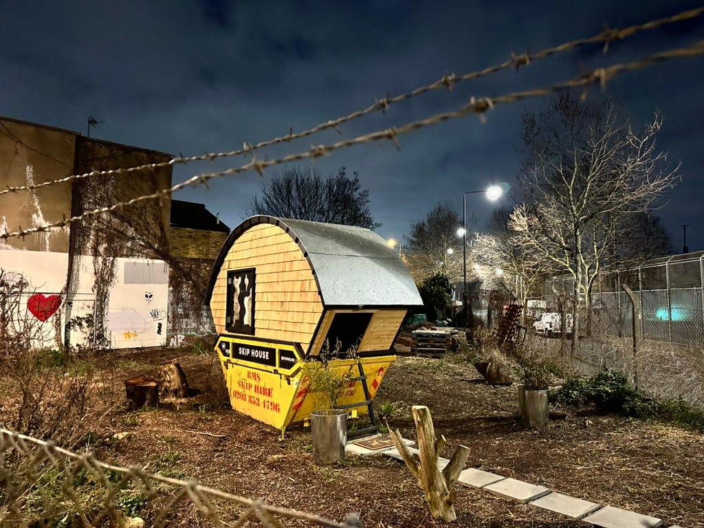 Another photo of the site where Stompie the tank used to be. For a short time during the pandemic, the tank was taken away and a modified skip took its place, which had had a wooden structure built on top of it. It was named Skip House and housed a young man for a few months as a commentary on the escalating cost of living in London.