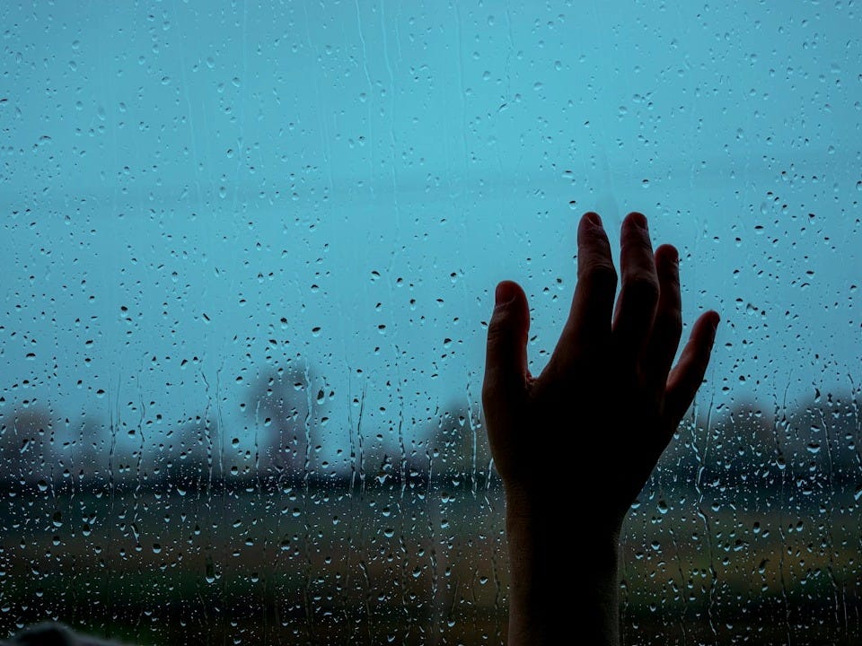 a person's hand reaching out of a window in the rain