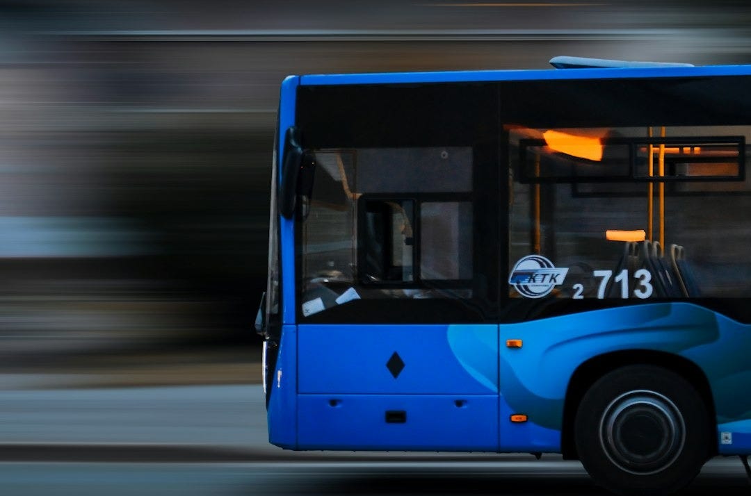 a blue bus driving down a street next to a tall building