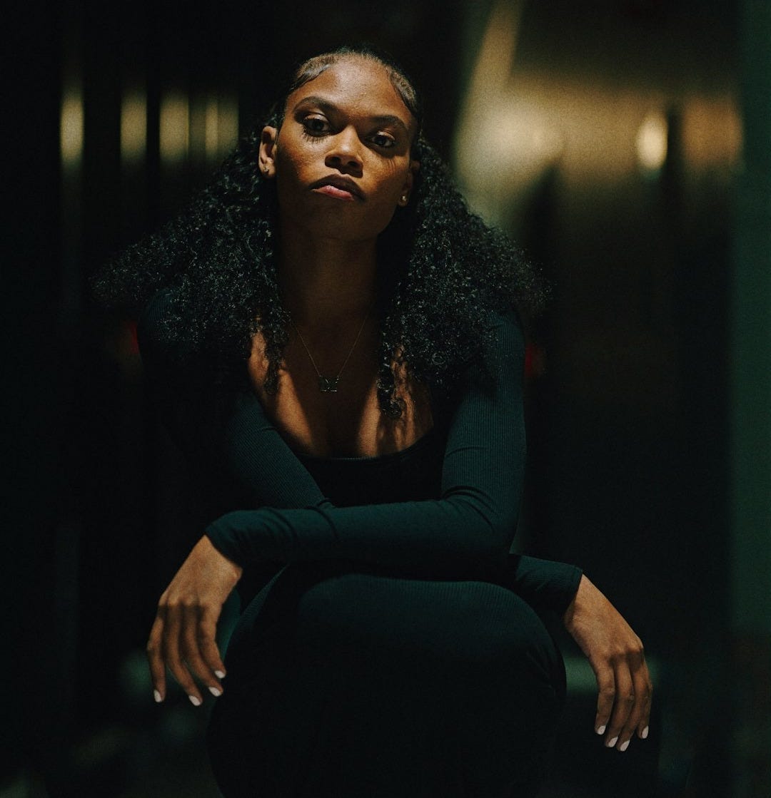 Young woman in black dress squats in dark hallway