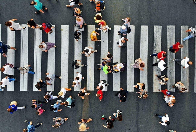 Aerial view of a busy crosswalk with many people walking in different directions across the striped pedestrian crossing. Aerial view of a busy crosswalk with many people walking in different directions across the striped pedestrian crossing.