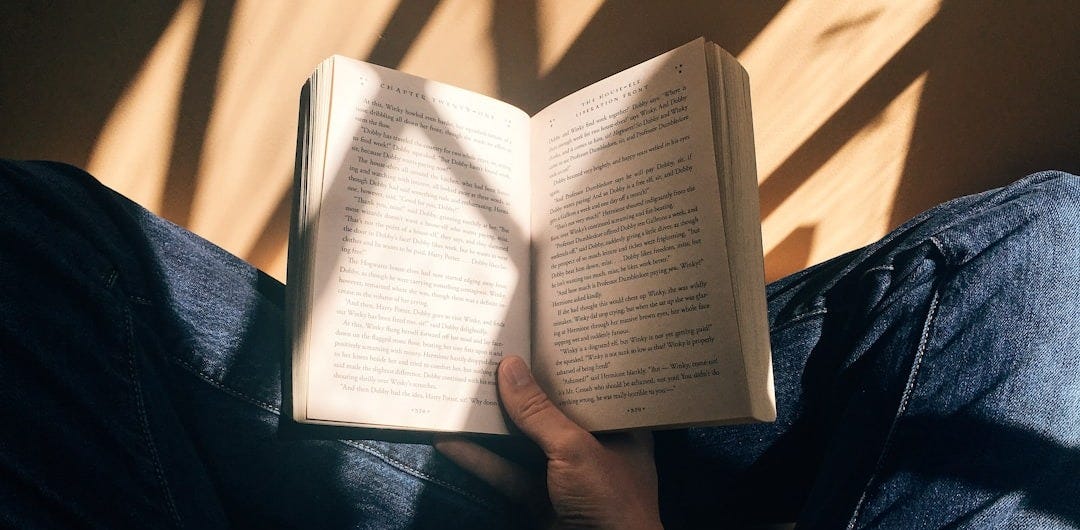 person holding book sitting on brown surface person holding book sitting on brown surface