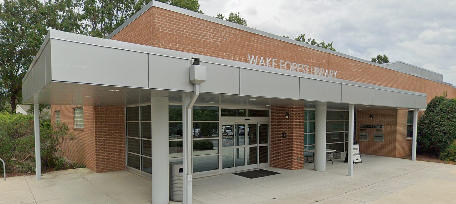 The main entrance of the Wake Forest Library, a brick building with a large metal canopy, glass doors, and a "BOOK RETURN" slot.