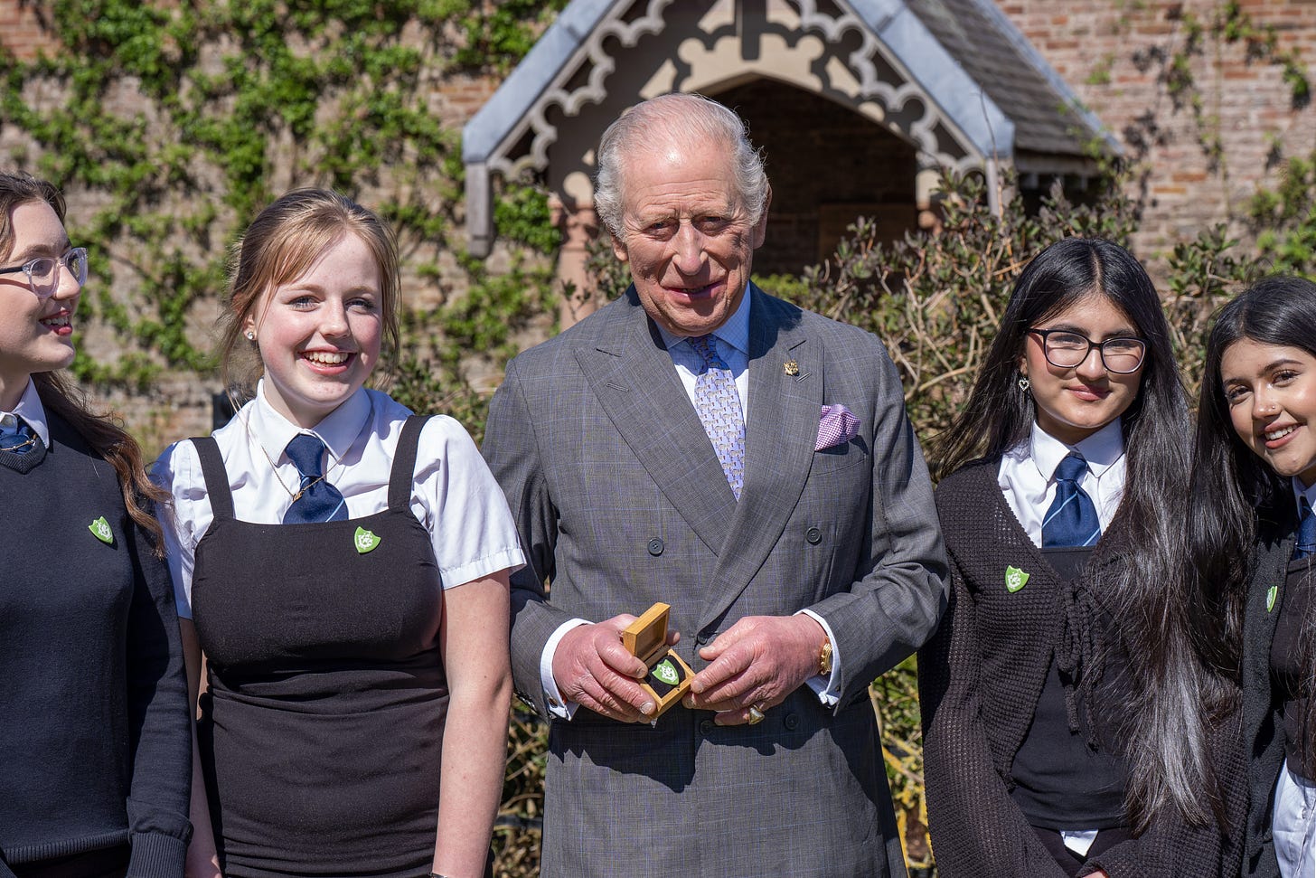 King Charle's holding a green Blue Peter badge next to school children