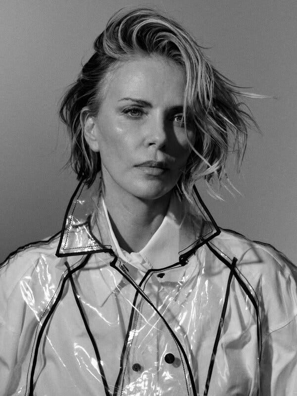 A black-and-white portrait of Theron wearing a clear plastic jacket over a collared shirt.