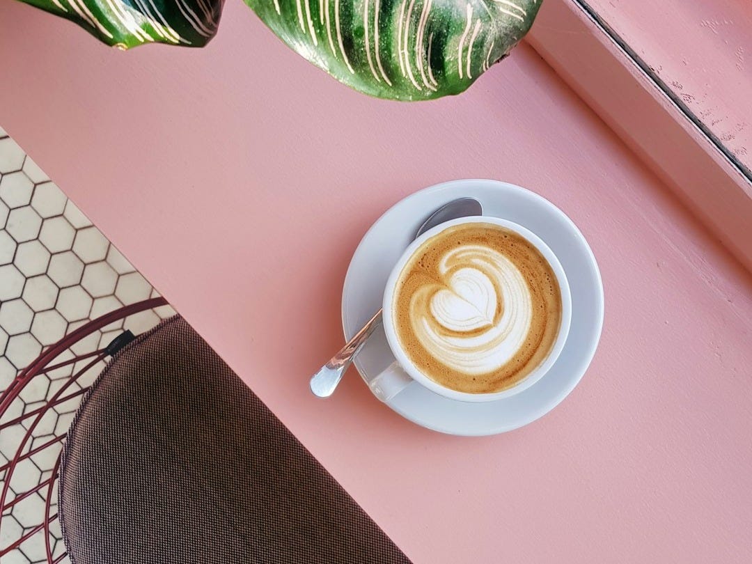 cup of coffee on saucer with teaspoon on pink tabletop