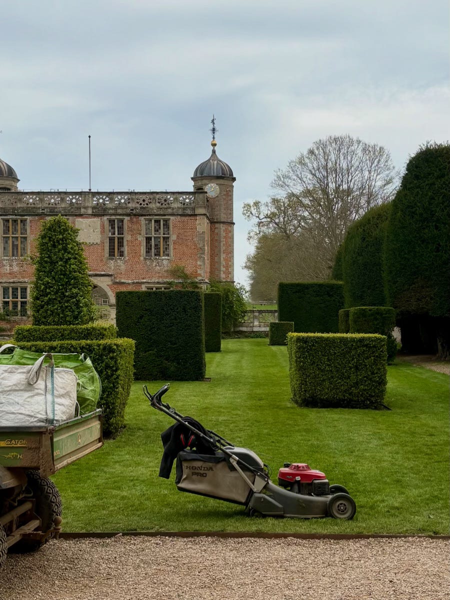 A lawn mower parked on the edge of a large lawn freshly mown, with topiary shrubs and Charlecote's Elizabethan gatehouse. A lawn mower parked on the edge of a large lawn freshly mown, with topiary shrubs and Charlecote's Elizabethan gatehouse.