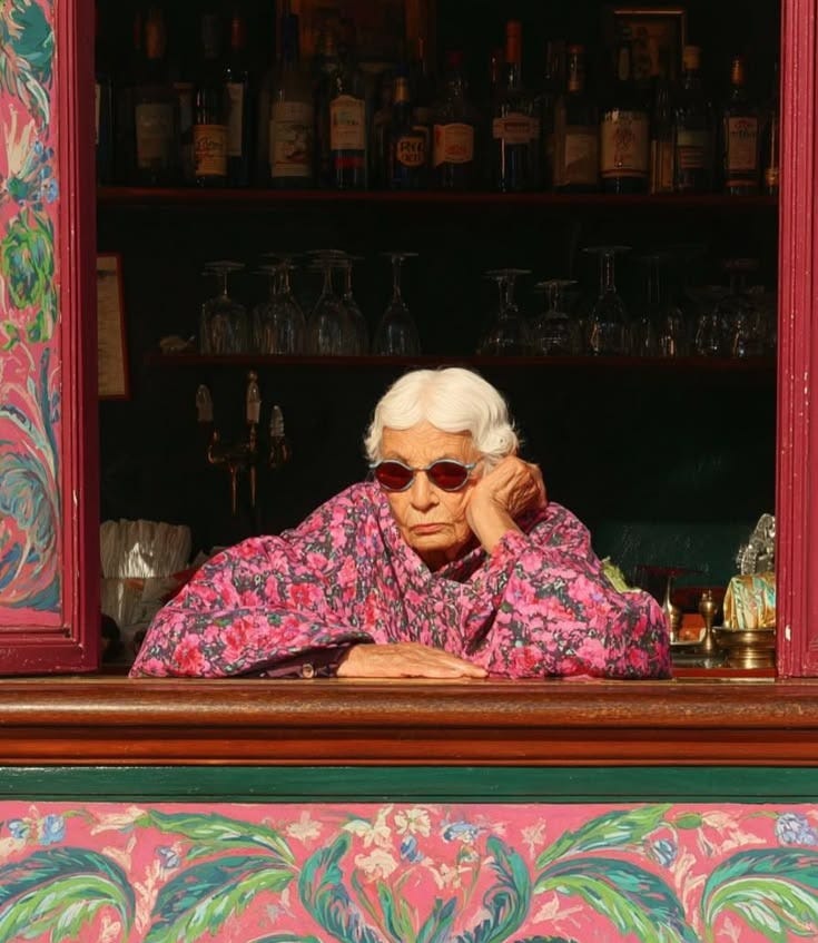This may contain: an older woman wearing sunglasses sitting at a window sill in front of a bar