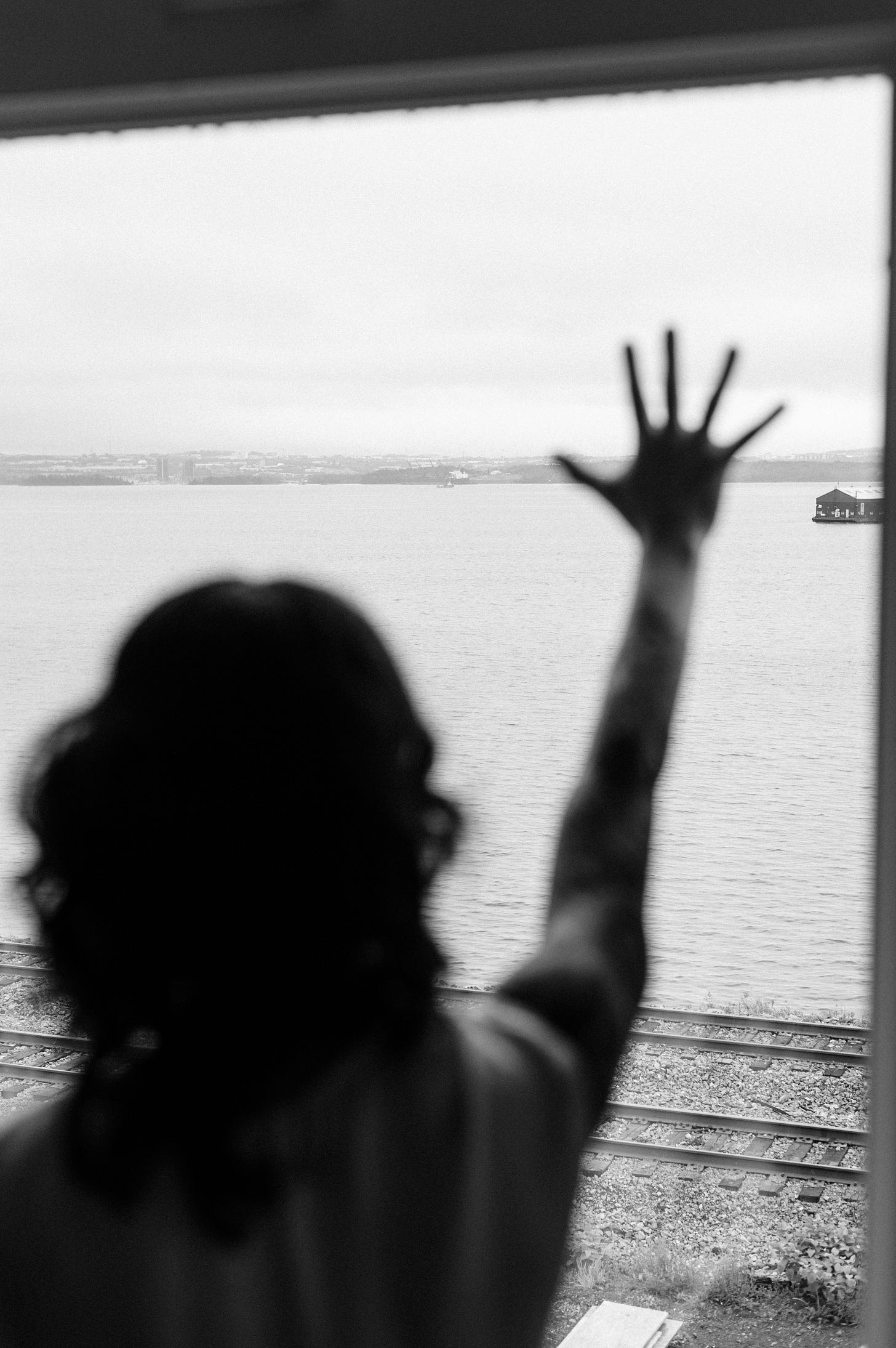 Author looking out over water through a large window while placing one hand on the glass