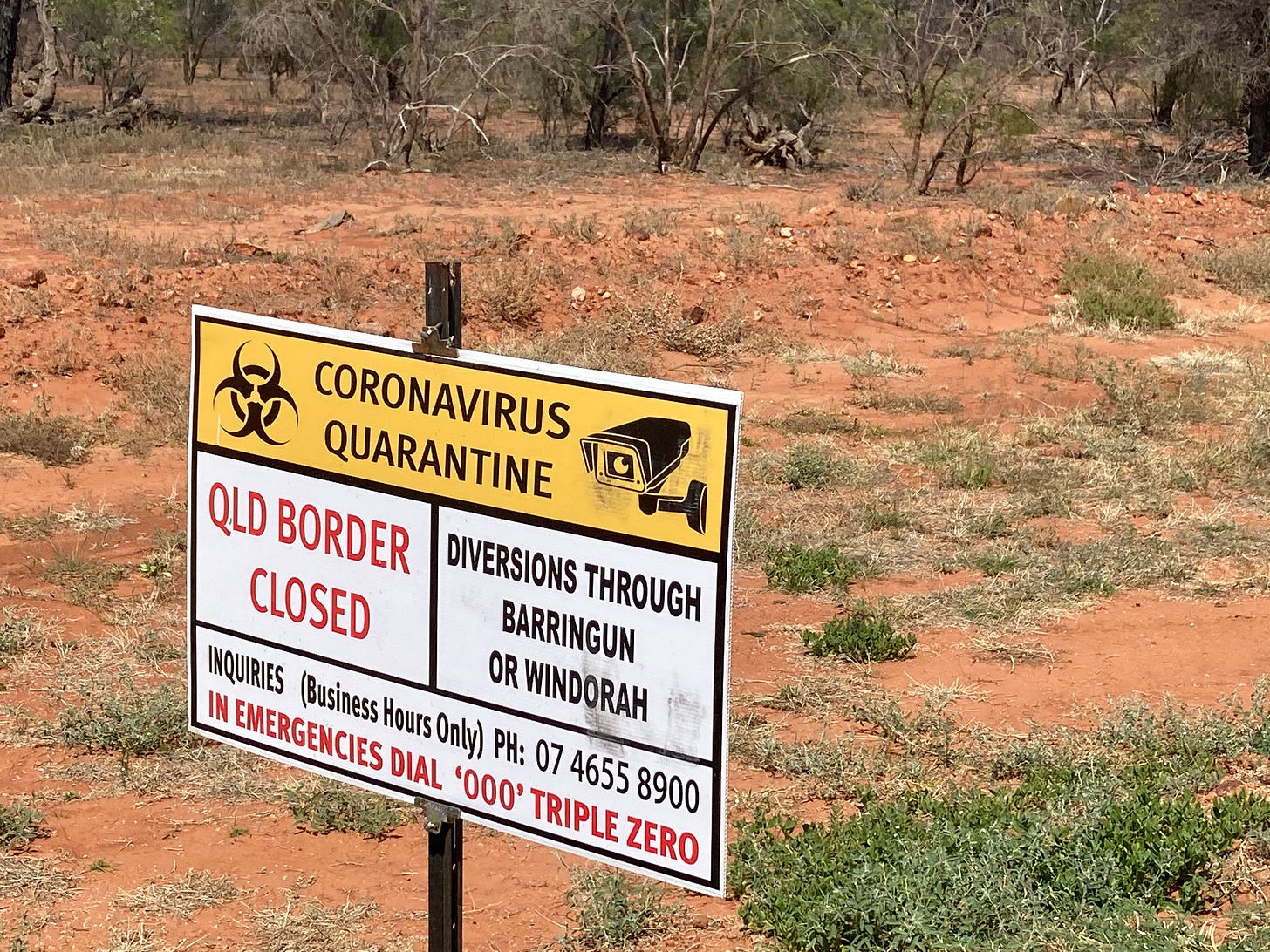 A yellow road sign in outback Queensland reading "Queensland Border Closed - Coronavirus Quarantine" under a security camera.