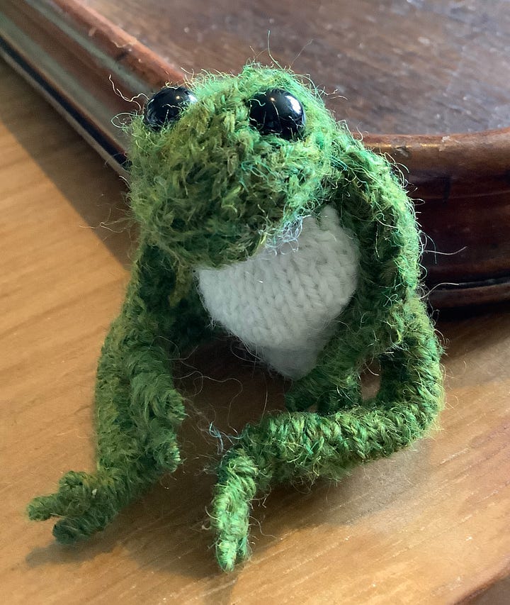 A green frog, with a cream chest, black eyes and a cheeky look. Sitting in a variety of positions, including lying on his back.