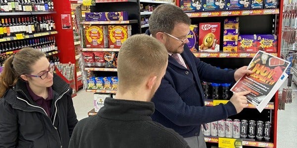 Business crime officer and a licensing officer with retail staff displaying a poster in the store window
