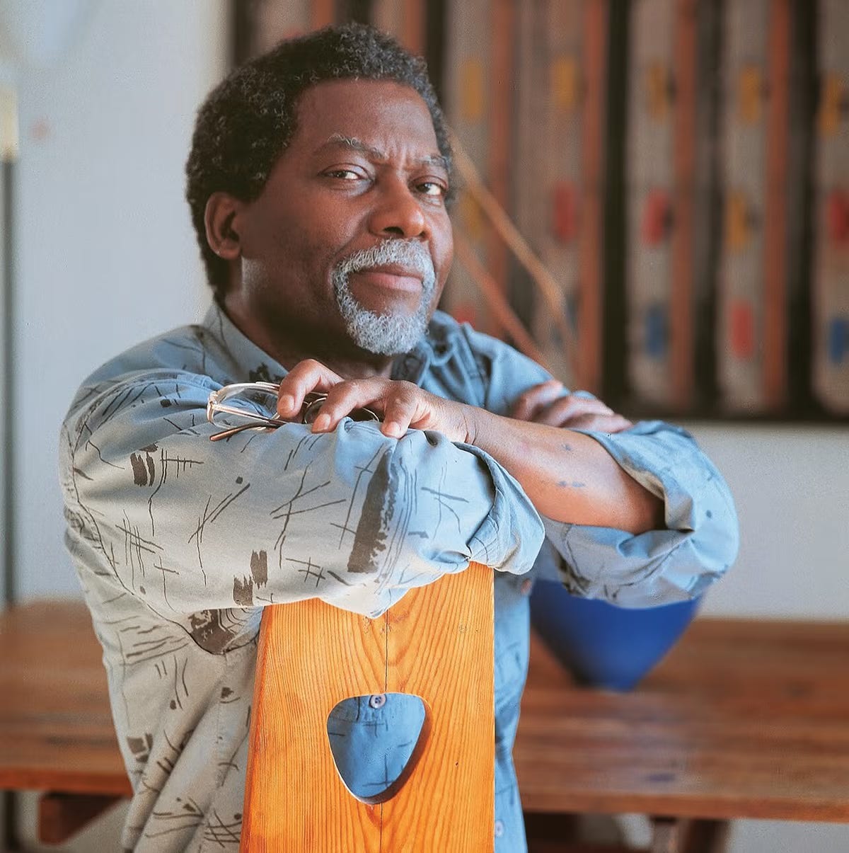Portrait of Howard Smith, holding his glasses in one hand as he sits against the backside of a wooden chair.