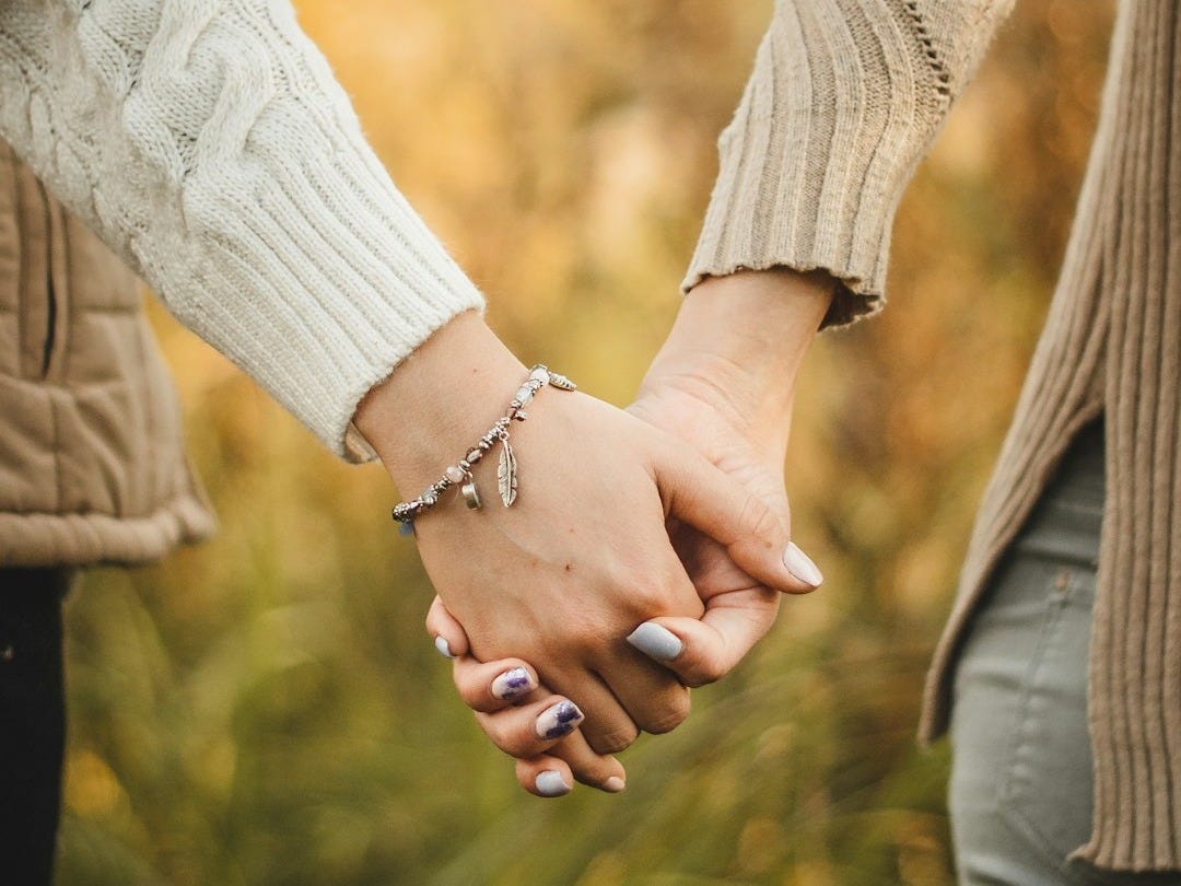 woman in white knit sweater holding hands with man in brown jacket