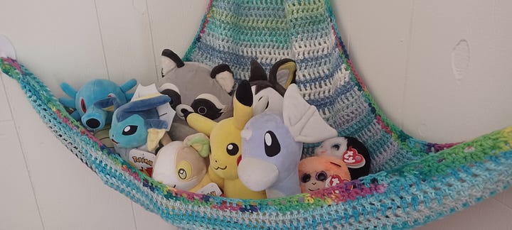 A crocheted toy hammock; the yarn is Lily's Sugar 'N Cream. The hammock has stuffed animals in it; several of which are Pokémon themed.