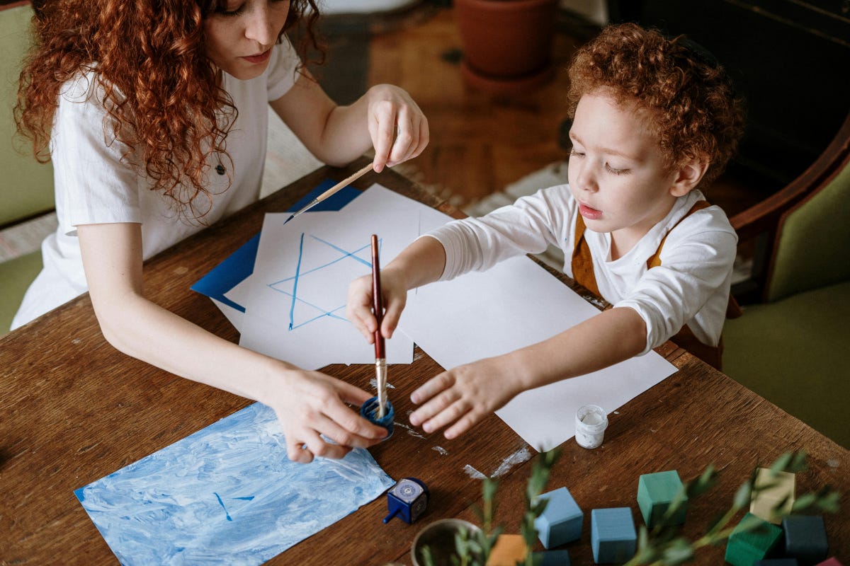 A very young child painting stars of David in blue with his mother's help