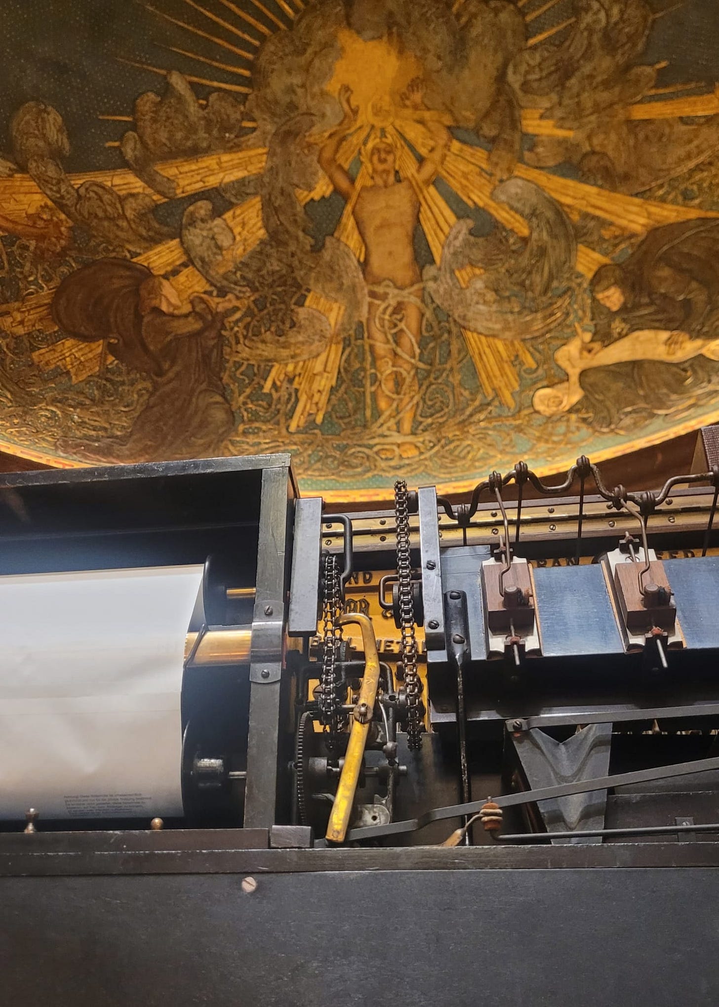 The mechanism of a player piano in close-up, with Gerald Moira's mural of 'The Soul of Music' one the ceiling of the Wigmore Hall stage in the background.
