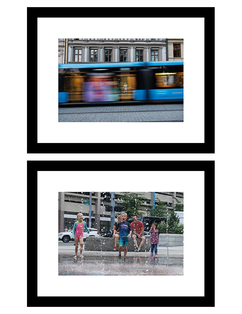 Two framed prints: blurred blue tram in Oslo and children playing in Boston fountains, shown together in gallery display Two framed prints: blurred blue tram in Oslo and children playing in Boston fountains, shown together in gallery display