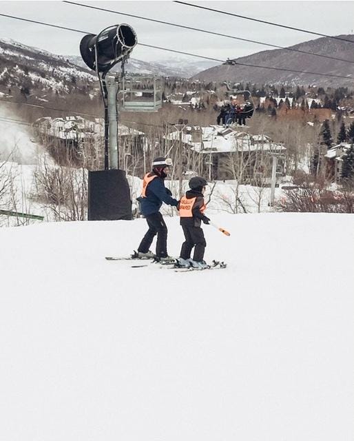 Ashton and his ski guide heading down the mountain. They are wearing bright orange vests. One reads Guide, the other says Visually Impaired. Ashton and his ski guide heading down the mountain. They are wearing bright orange vests. One reads Guide, the other says Visually Impaired.