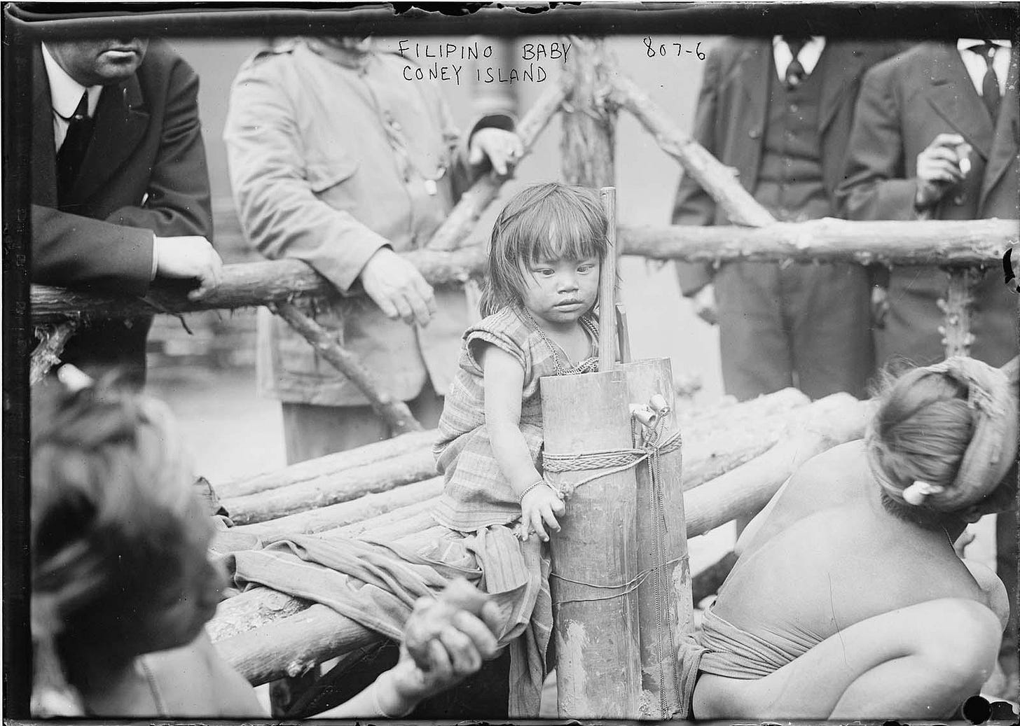 A young Filipino girl is pictured sitting on a wooden bench in an enclosure and "displayed" in Coney Island. New York, 1905.