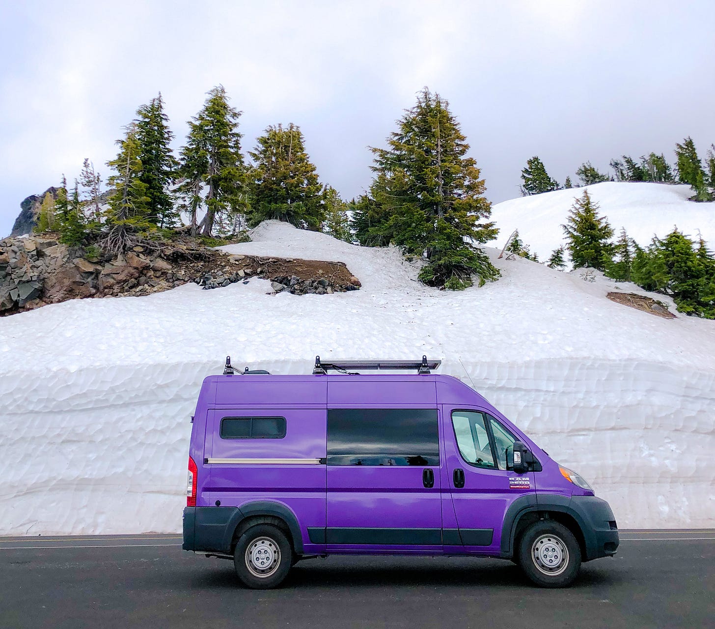 A purple van parked on a road in front of a tall wall of snow. A purple van parked on a road in front of a tall wall of snow.