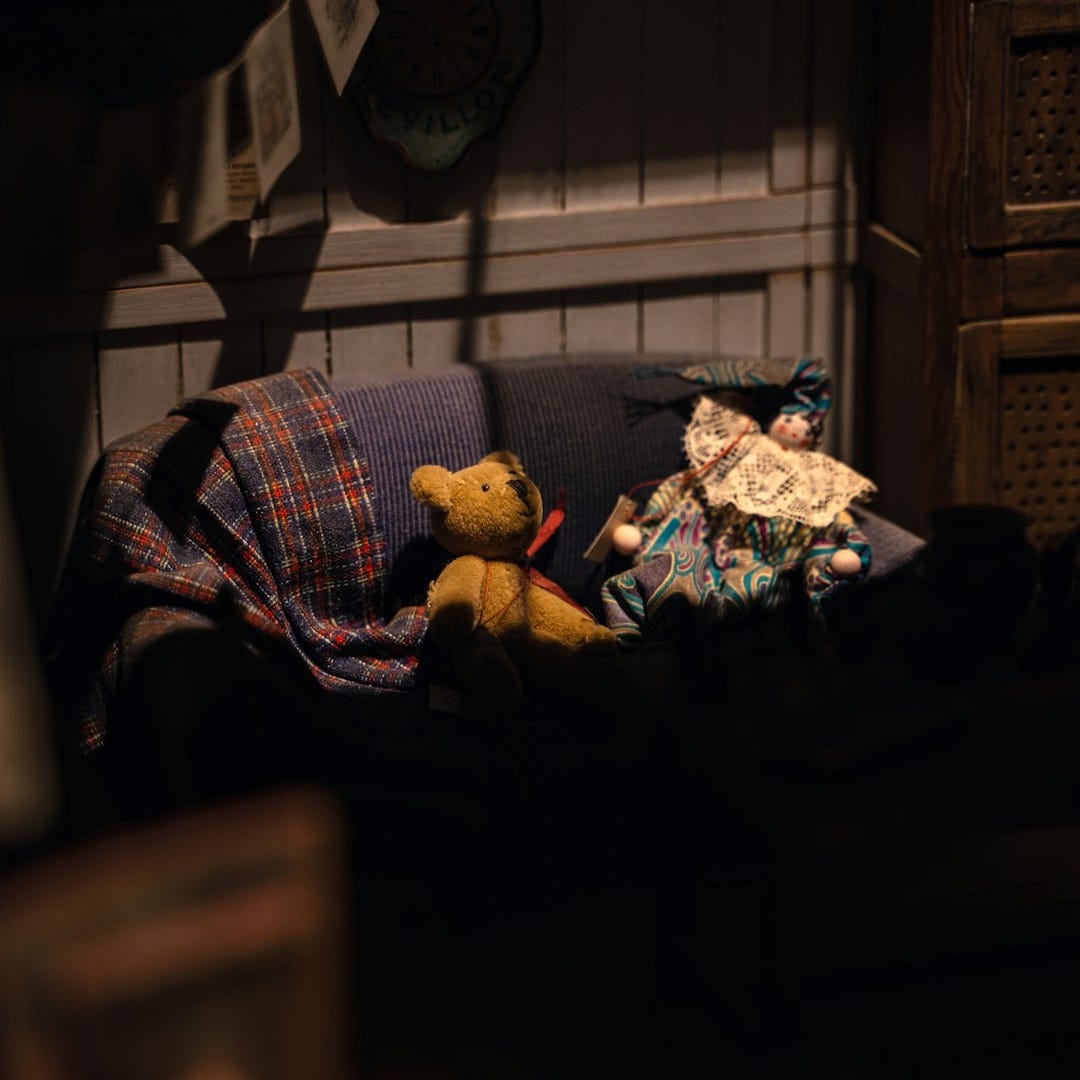 a teddy bear sitting on a couch in a dark room a teddy bear sitting on a couch in a dark room