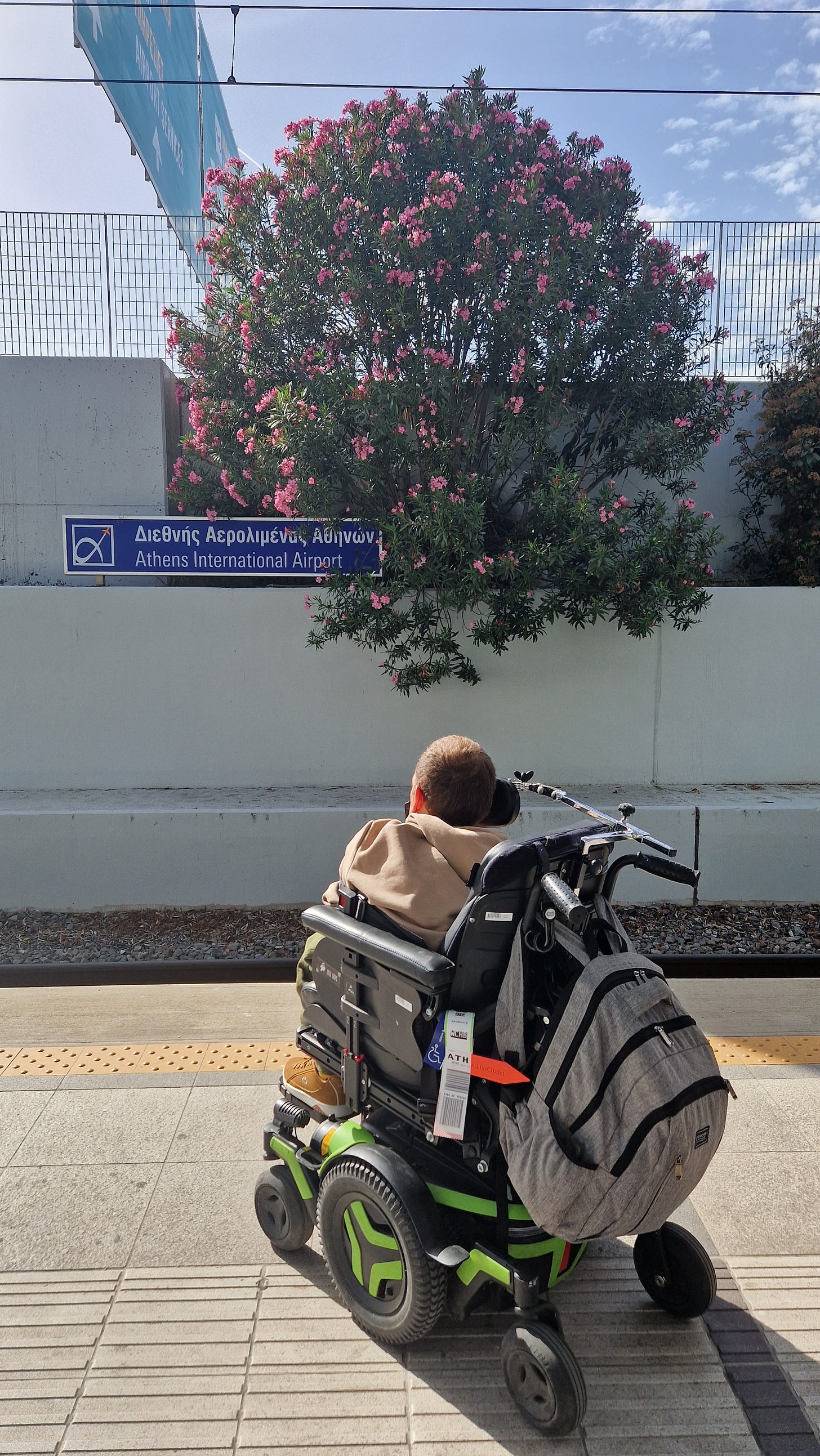 Me waiting on the platform at the Athens International Airport metro station. In the background a large pink flowering shrub.