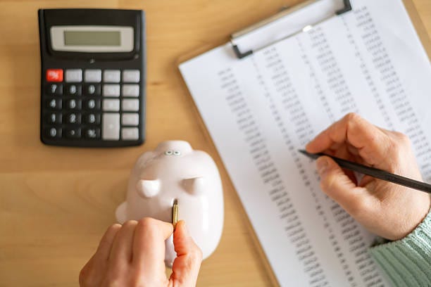 Accountant inserting a coin into piggy bank and calculating expenses with calculator and spreadsheet on a wooden desk, managing home budget and savings Accountant inserting a coin into piggy bank and calculating expenses with calculator and spreadsheet on a wooden desk, managing home budget and savings financial workseet stock pictures, royalty-free photos & images