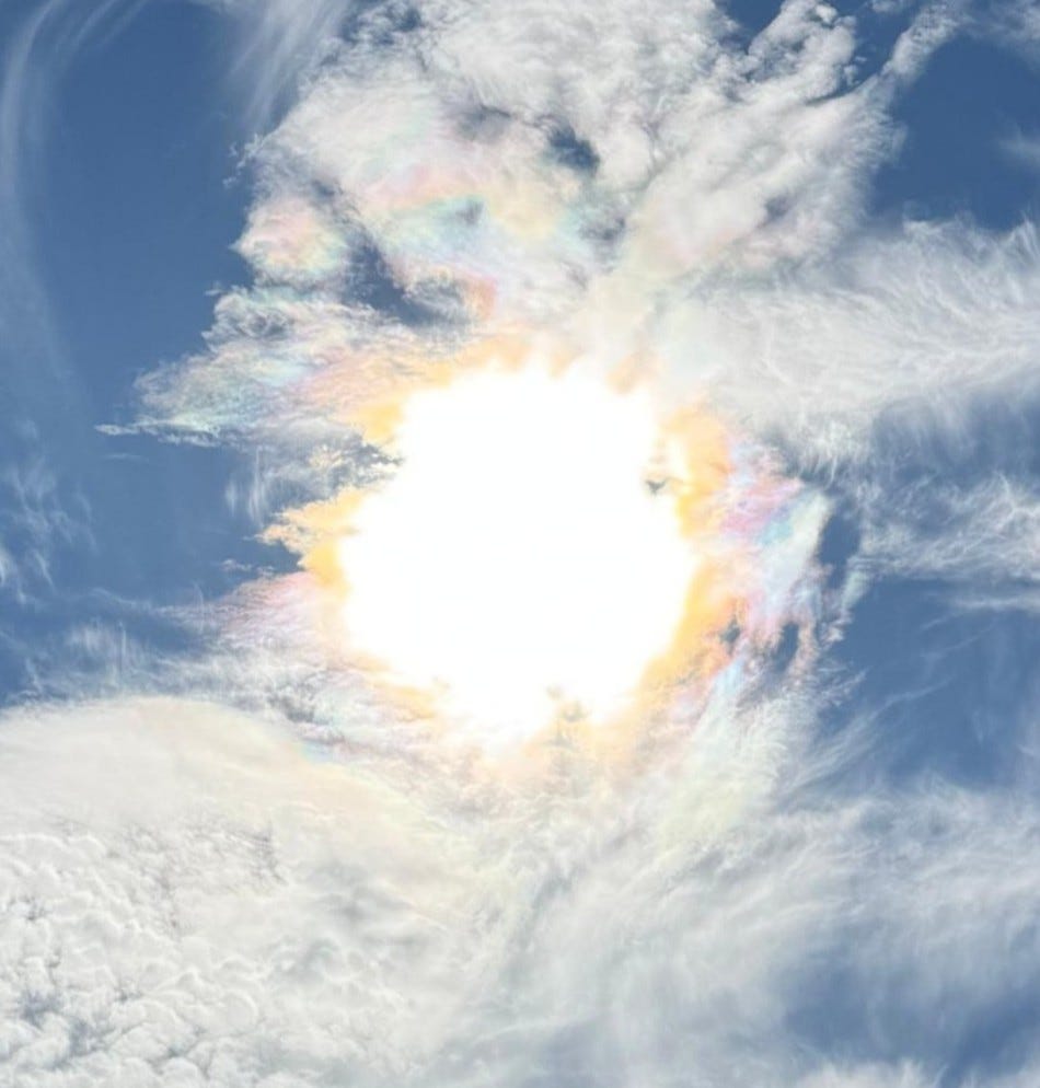 Photo en gros plan d'un soleil d'automne recouvert d'un tourbillon de nuages blancs sur un ciel bleu, le soleil ressemble à une boule de feu diffuse entouré d'un halo arc-en-ciel