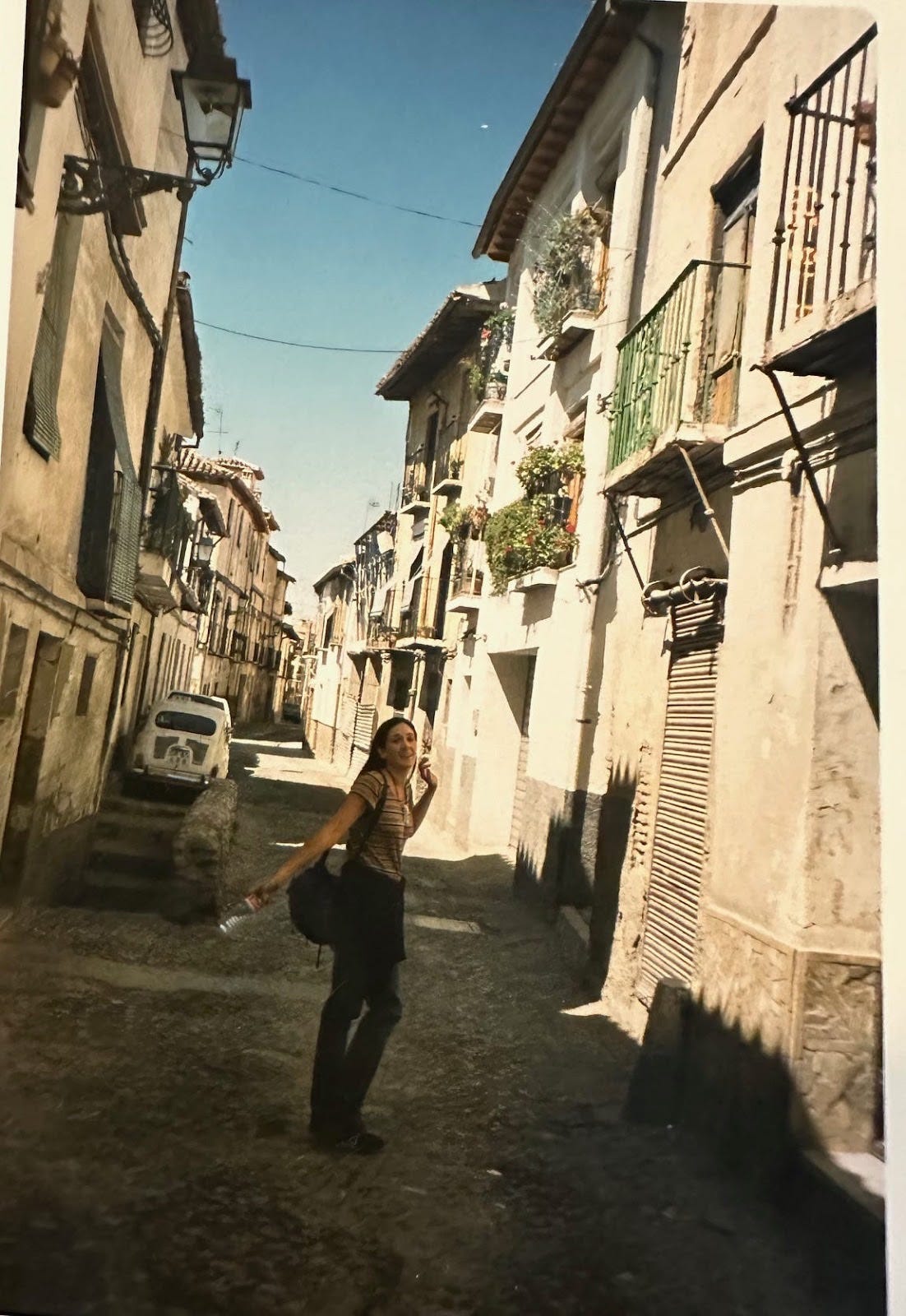 A young woman stands in an old, cobbled street in Spain, looking back at the camera