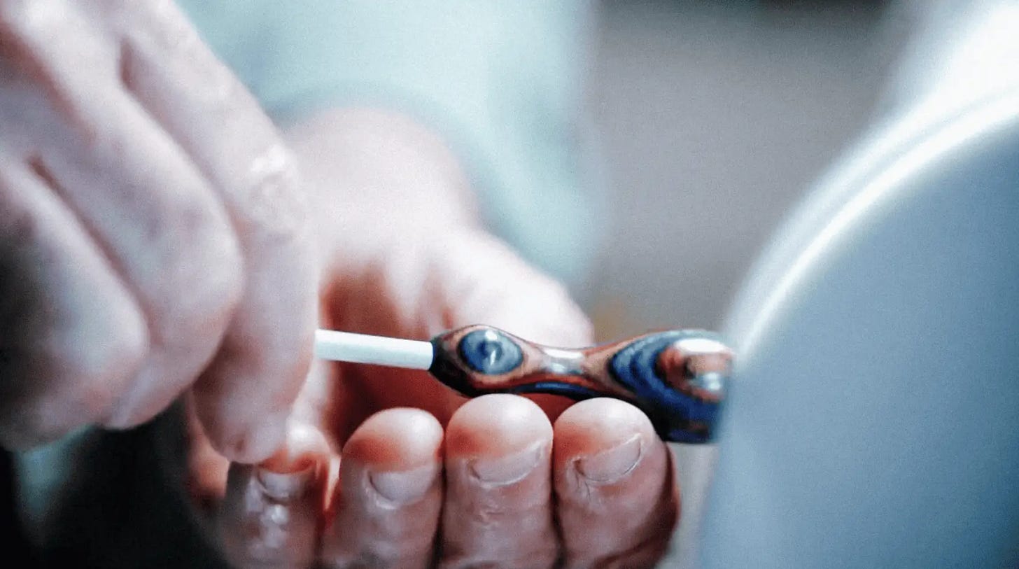 Closeup of a craftsman's hands holding the wooden bulb of a handmade conducting baton against a sander.