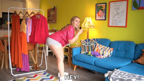 Hannah wearing a sparkly top and short shorts, bending over and saying hey