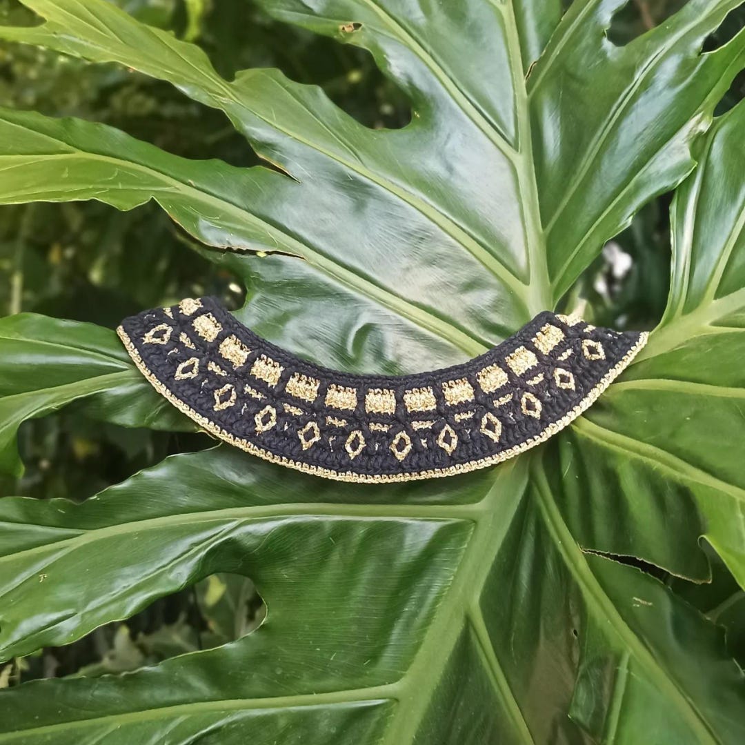 Black and gold mosaic crochet necklace with big leaves at the background. Black and gold mosaic crochet necklace with big leaves at the background.