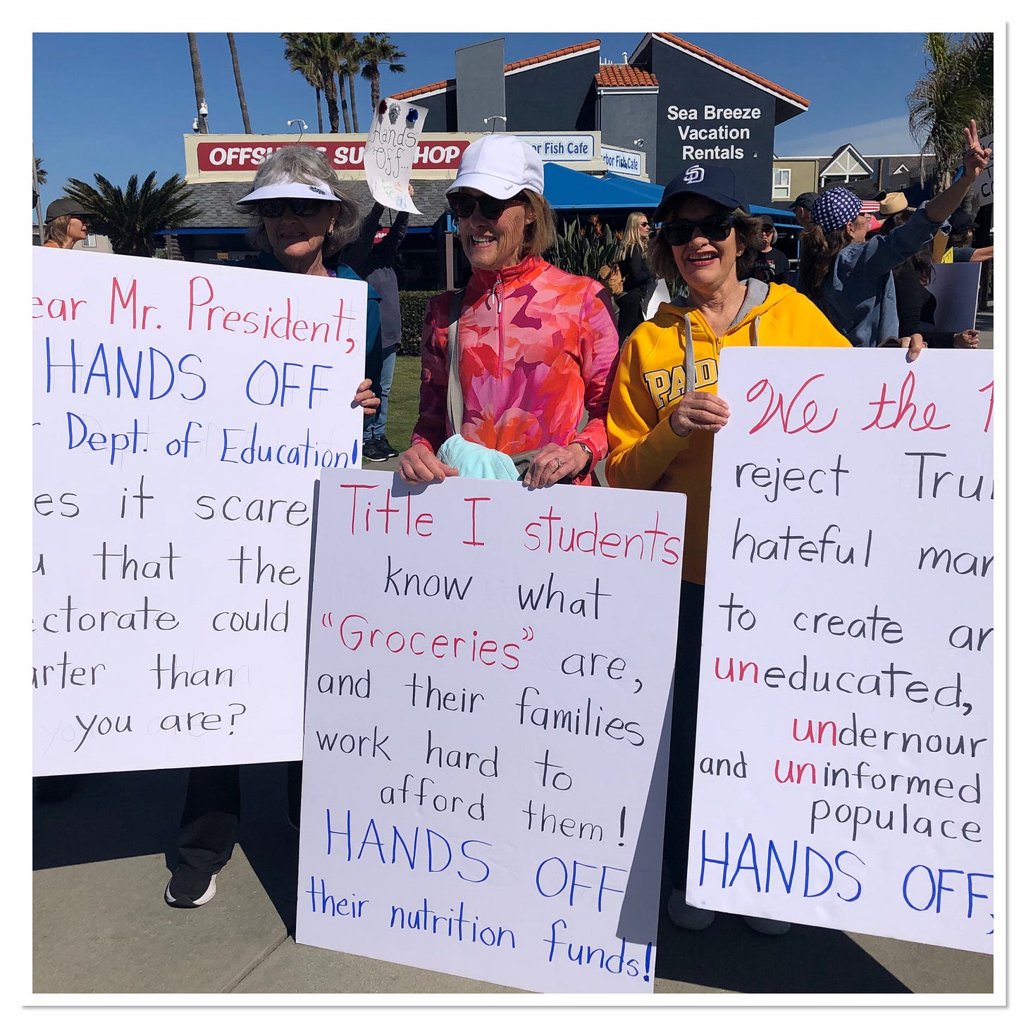 Poster holing sign that says “Title I students know what groceries are, and their families work hard to afford them! HANDS OFF their nutrition funds!”