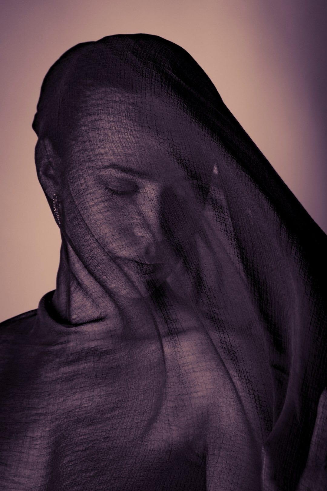 Woman's face covered with sheer purple fabric
