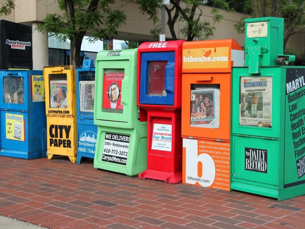 Multiple newspaper dispensers lined up on a street in Baltimore, Maryland.
