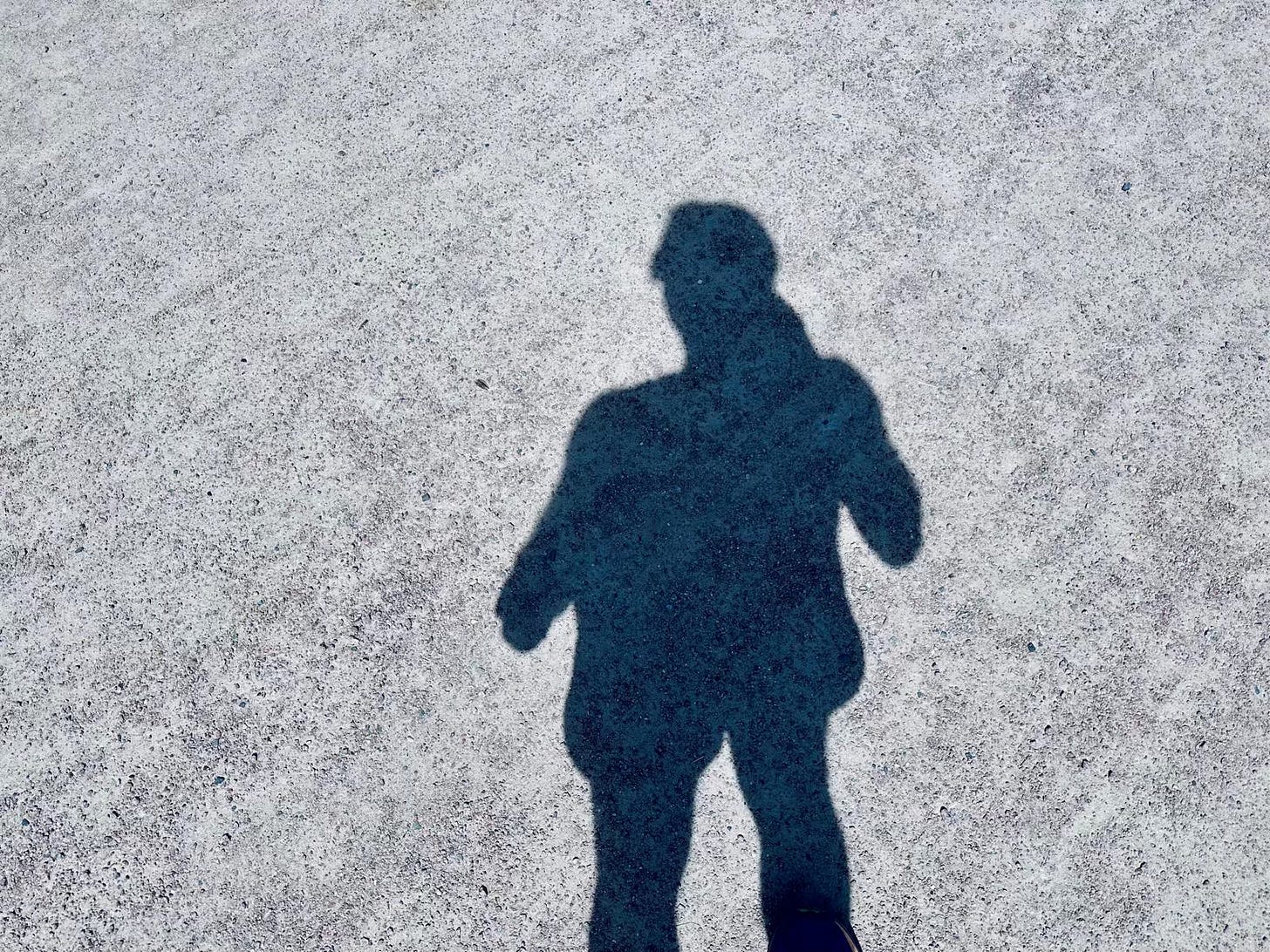 A long shadow cast on pavement on a sunny day, the person it belongs to outside the frame.