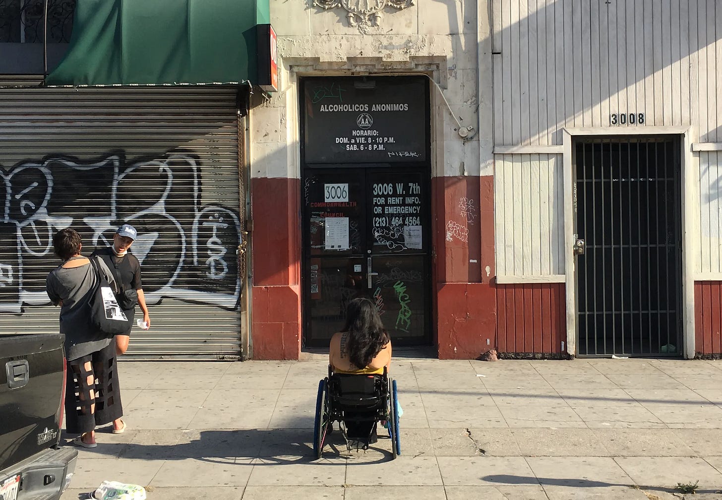 On a sunlit street, a wheelchair-using artist faces an entry to an inaccessible building.