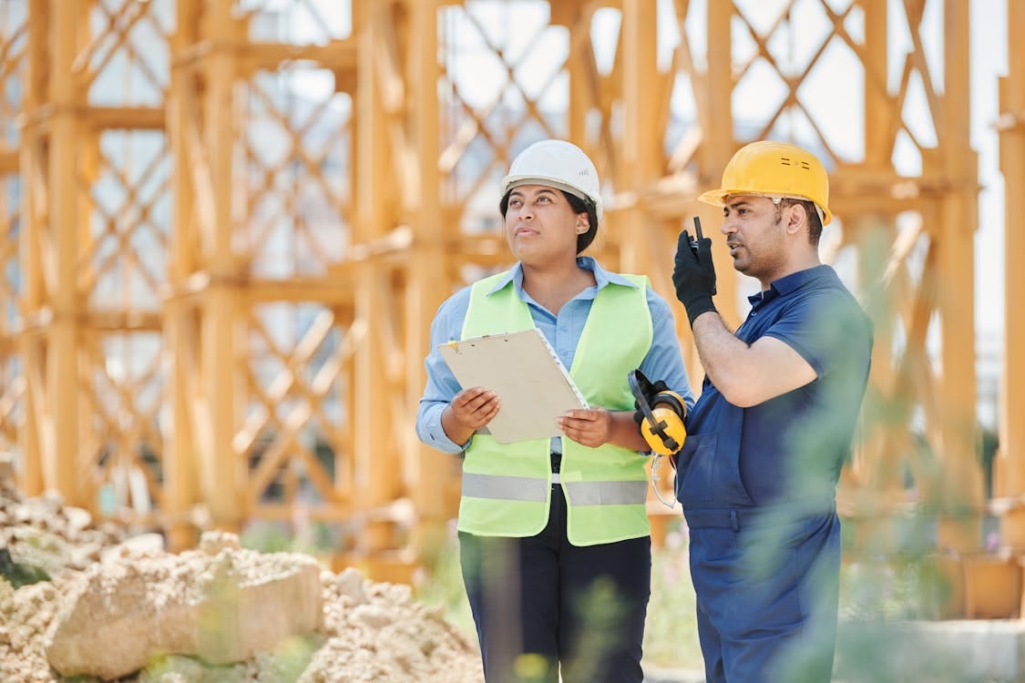 Free Male and female construction workers in protective gear discussing plans at an outdoor site. Stock Photo