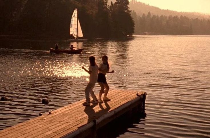 This may contain: two people are running on a dock near the water and sailboats in the distance