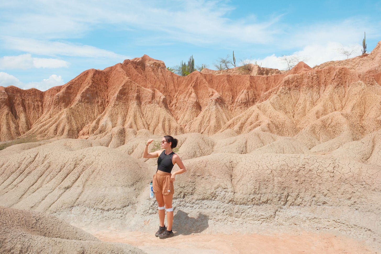 Woman standing in the Tatacoa Desert, Colombia, shielding her eyes against striped orange and grey eroded rock formations.