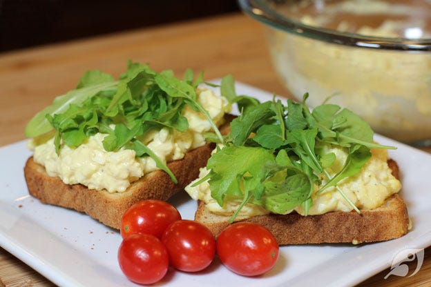 Egg salad spread on toast with baby lettuce and microgreens, served on a plate with grape tomatoes. Egg salad spread on toast with baby lettuce and microgreens, served on a plate with grape tomatoes.