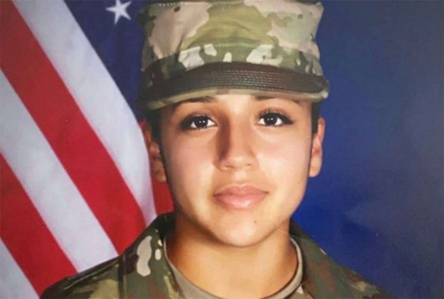 Vanessa Guillén, a young Army private wearing green camo fatigues, stands in front of a US flag in a portrait photo