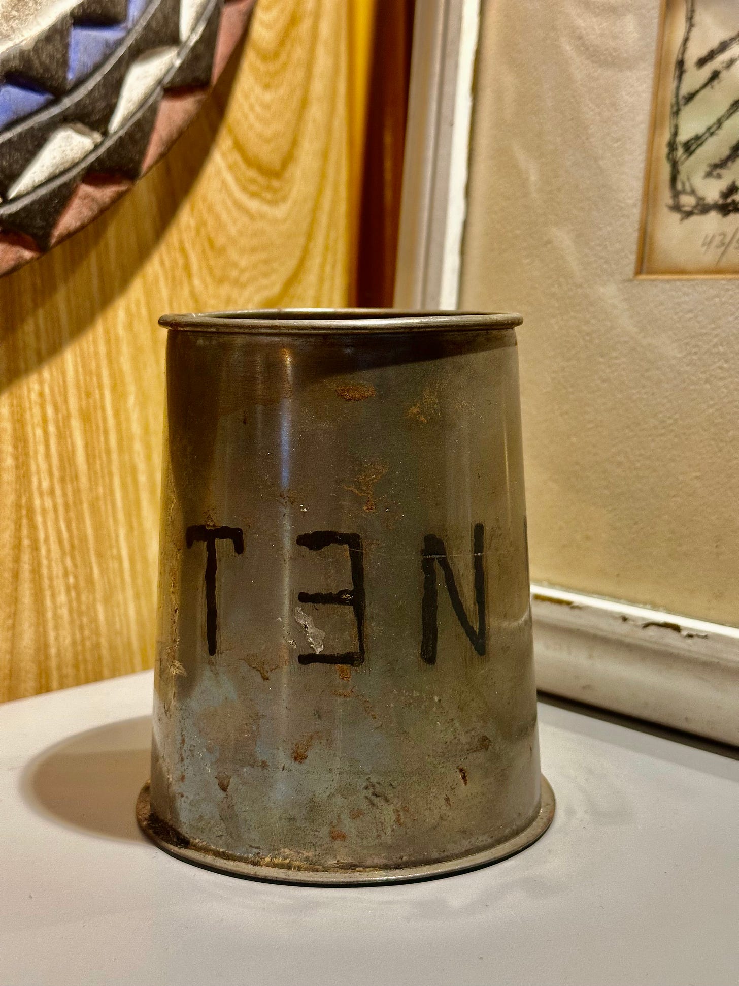 photograph of a dirty tin tankard cup with the word TEN on it with the E backwards