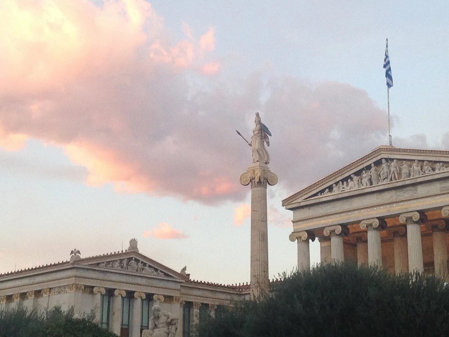 A statue of Athena stands on top of a pillar outside of an ancient Greek-style building