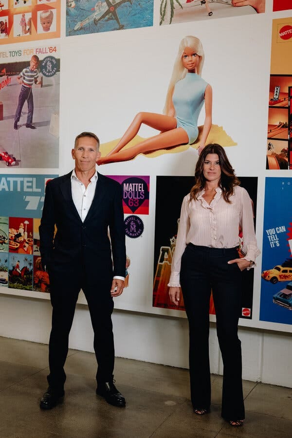 Ynon Kreiz and Robbie Brenner, each with one hand in a pants pocket, stand in front of a wall full of Barbie and other Mattel images. Ynon Kreiz and Robbie Brenner, each with one hand in a pants pocket, stand in front of a wall full of Barbie and other Mattel images.