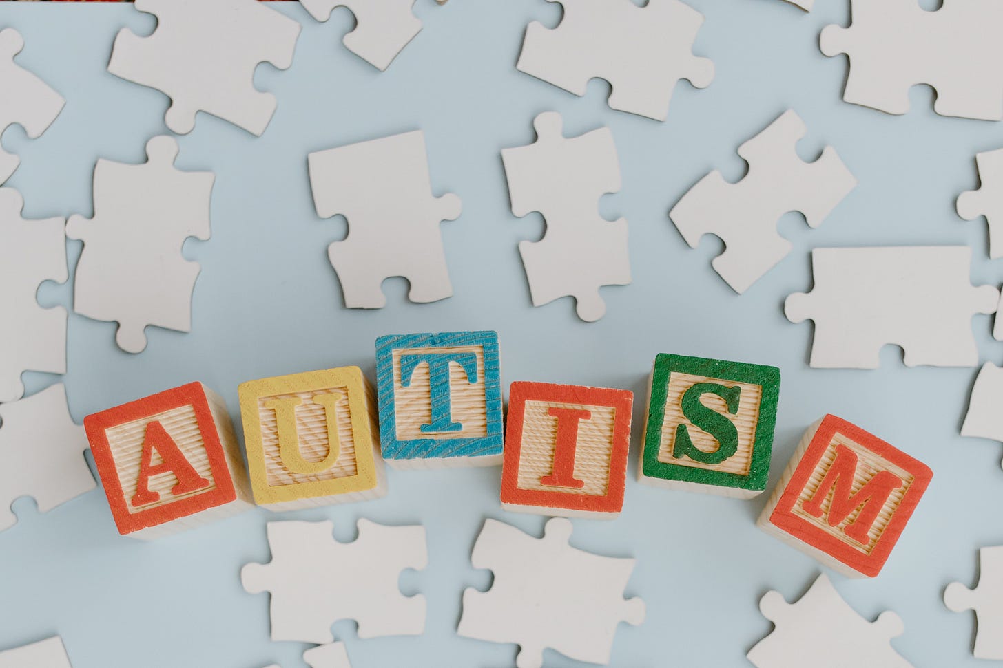 the word Autism spelled out in blocks with white puzzle pieces scattered around it