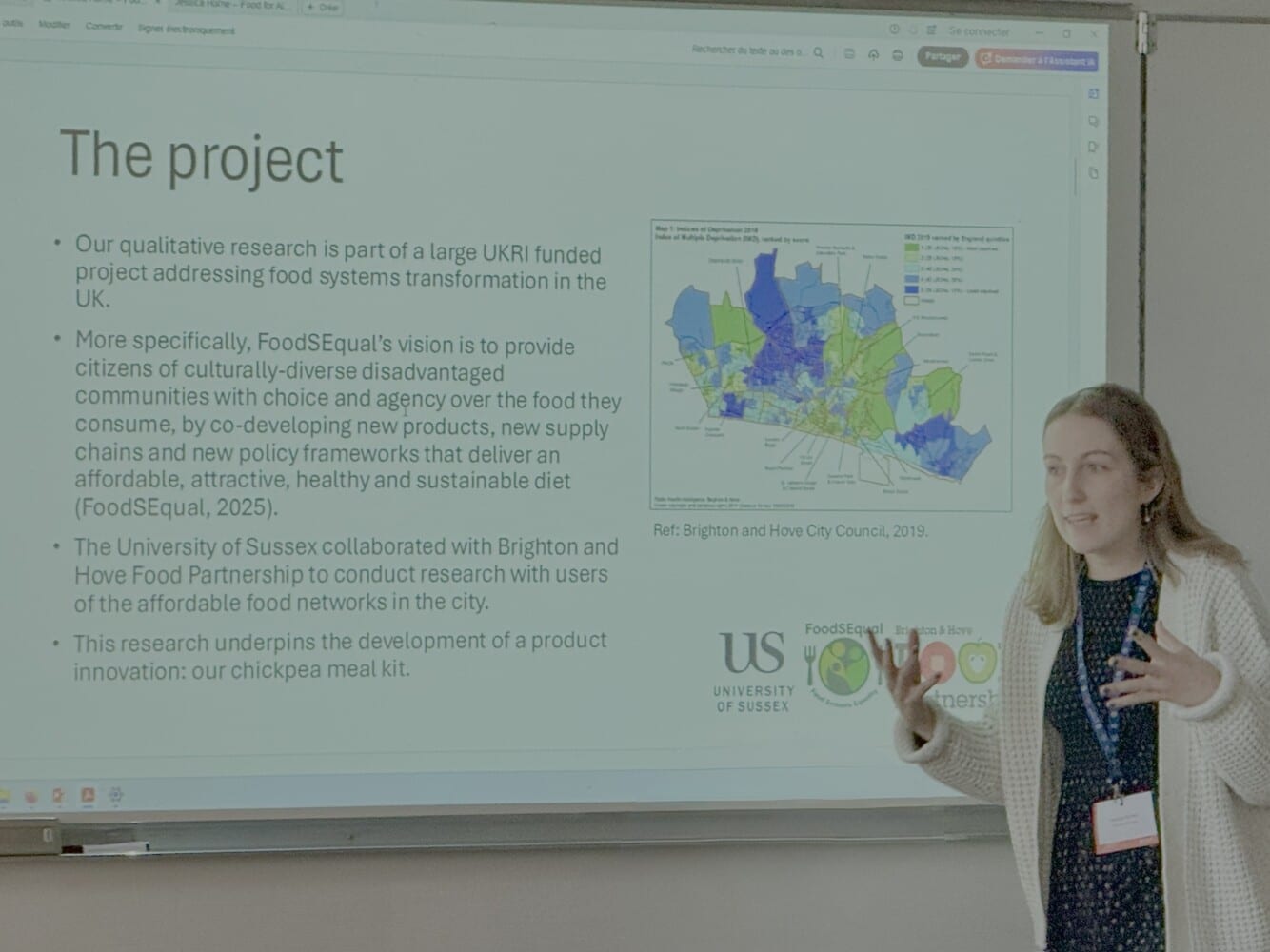 Woman in front of screen giving a presentation. Slide title: "The project" followed by 4 bullets describing a qualitative project examining the development of a vegetarian meal kit. A map of the region is to the right of the text.